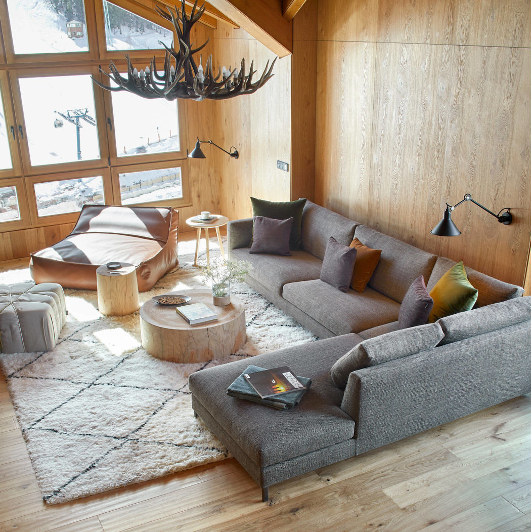 Cozy wooden cabin living room with a modern sofa and antler chandelier.