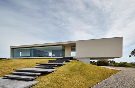 Minimalist cantilevered house with large glass windows and floating steps.