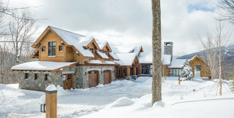 Snow-covered lodge with stone base and wooden upper in a wintry landscape.