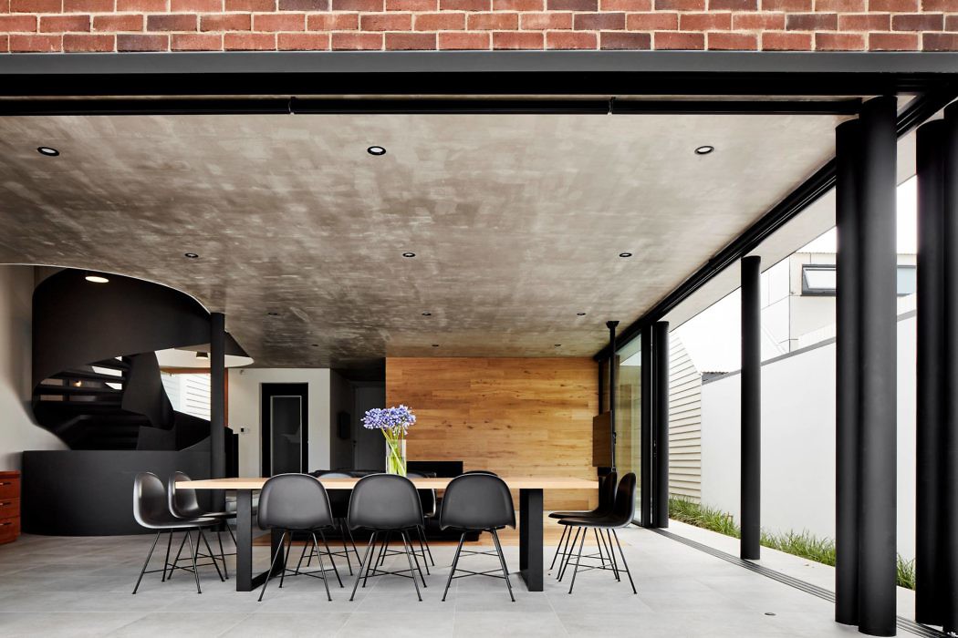 Modern dining area with exposed brick and concrete, black chairs, and large windows.