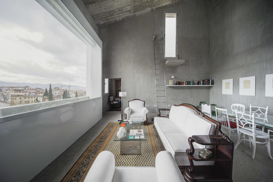 Minimalist interior with concrete walls, eclectic furnishings, and large window.