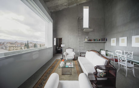 Minimalist interior with concrete walls, eclectic furnishings, and large window.