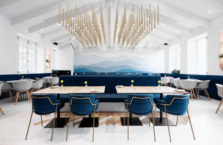 Modern dining room with blue chairs, wooden tables, and geometric ceiling light fixture.