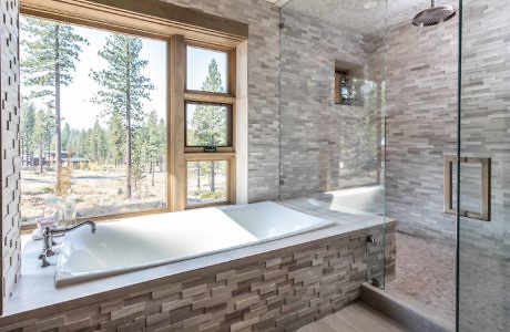 Modern bathroom with a large tub, glass shower, and forest view.