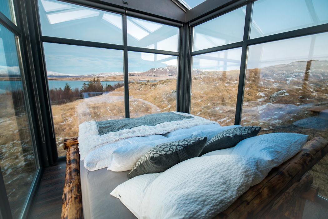 Bedroom with glass walls and scenic outdoor view.