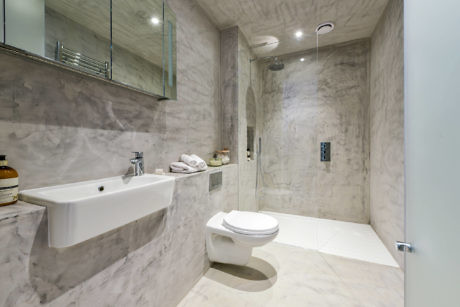 Modern bathroom with marble walls, walk-in shower, and white fixtures.