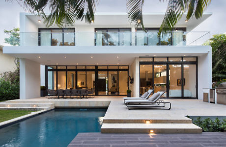 Modern two-story house with large windows, poolside patio, and loungers surrounded