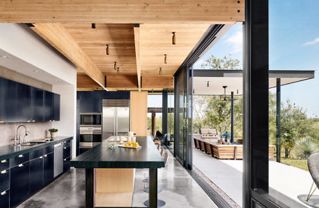 Modern kitchen interior with wooden ceiling and large windows overlooking a patio.