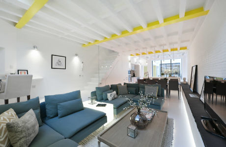 Modern living room interior with blue sofas, white walls, and yellow accents on ceiling