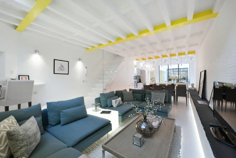 Modern living room interior with blue sofas, white walls, and yellow accents on ceiling