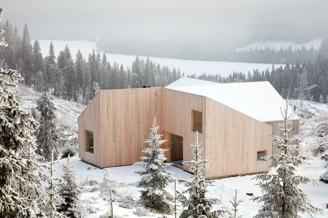 Contemporary wooden cabin in snowy landscape with trees.