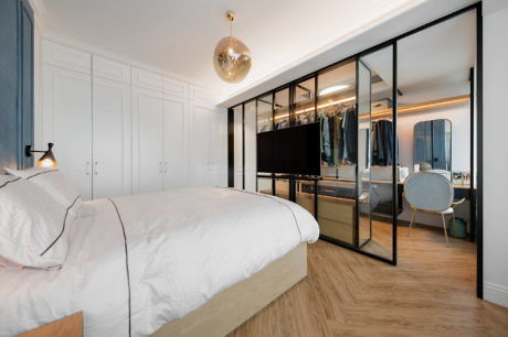 Modern bedroom with glass partition wardrobe and a golden pendant light.