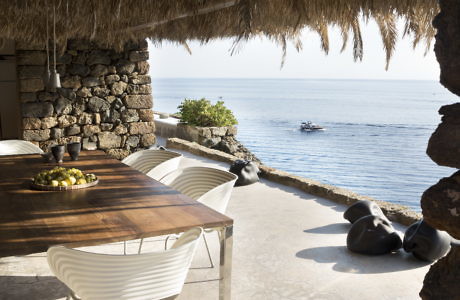 Outdoor dining area with a wooden table, modern chairs, and ocean view.