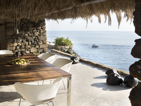 Outdoor dining area with a wooden table, modern chairs, and ocean view.