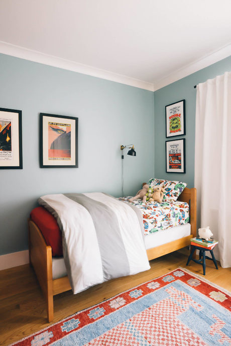 Cozy bedroom with blue walls, framed posters, and vibrant bedspread.