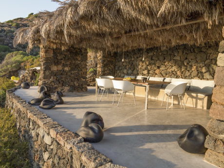 Rustic outdoor dining area with thatched roof and unique beanbag chairs.