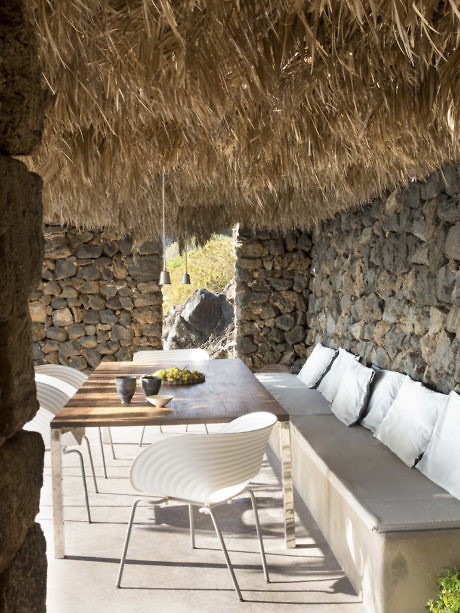 Outdoor dining area with thatched roof, stone walls, and a wooden table.