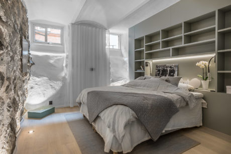 Modern bedroom with a bed, built-in shelves, and exposed rock wall, snow