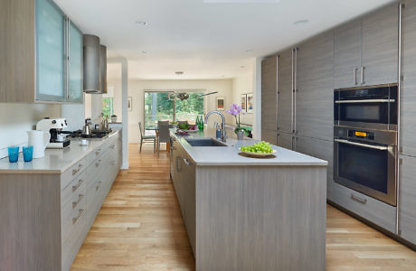 Modern kitchen interior with wood floors, gray cabinets, and stainless steel appliances.