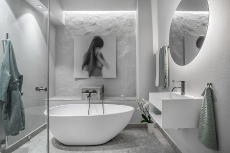 Contemporary white bathroom with oval bathtub and circular mirror.
