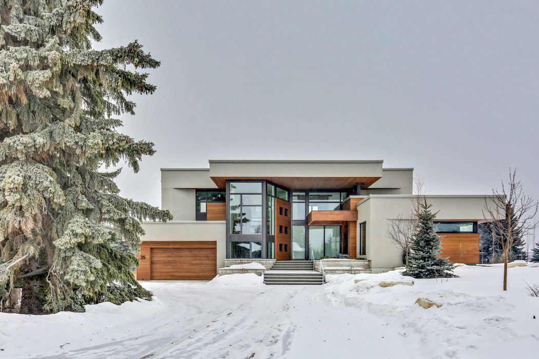 Modern house with large windows and wooden accents in a snowy landscape.