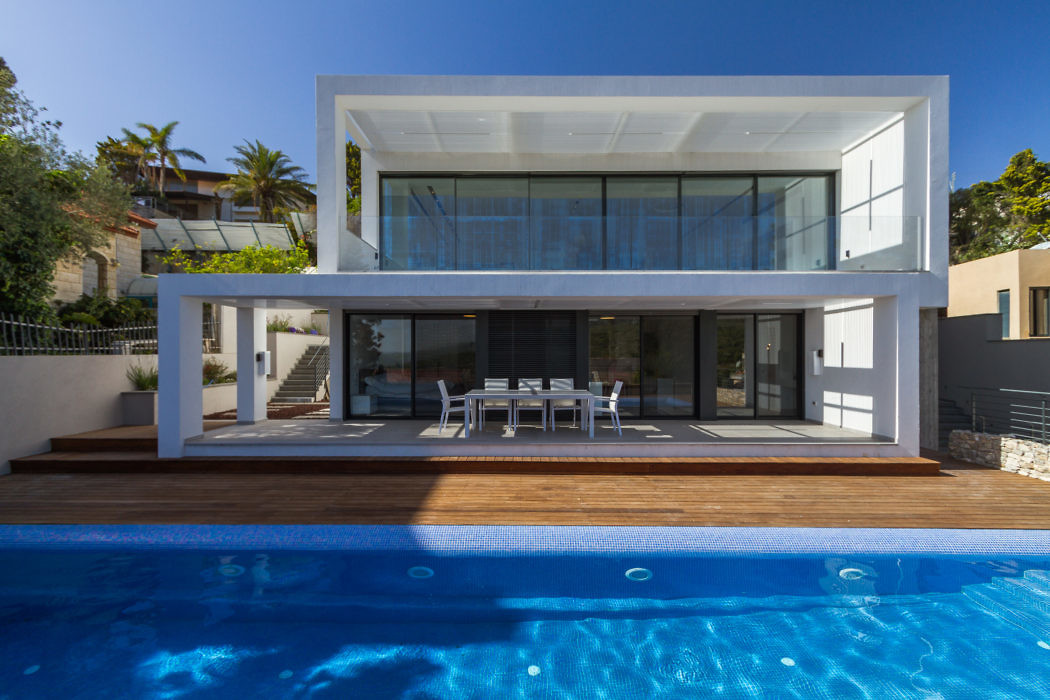Contemporary white villa with large windows, overlooking a pool.