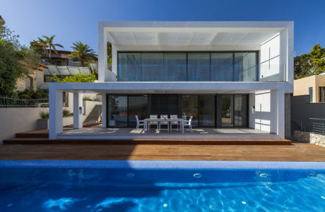 Contemporary white villa with large windows, overlooking a pool.