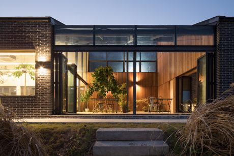 Contemporary brick house with large glass windows and warm interior lighting at dusk.