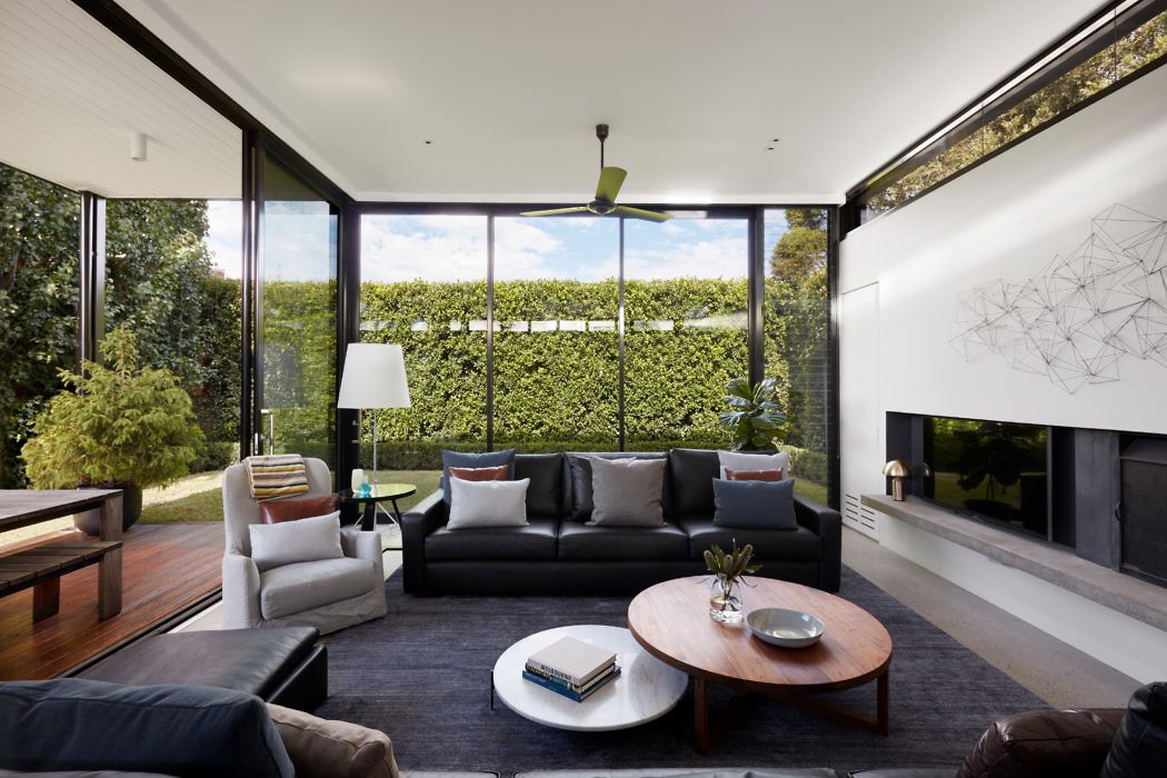 Modern living room with large windows and a hedge view.