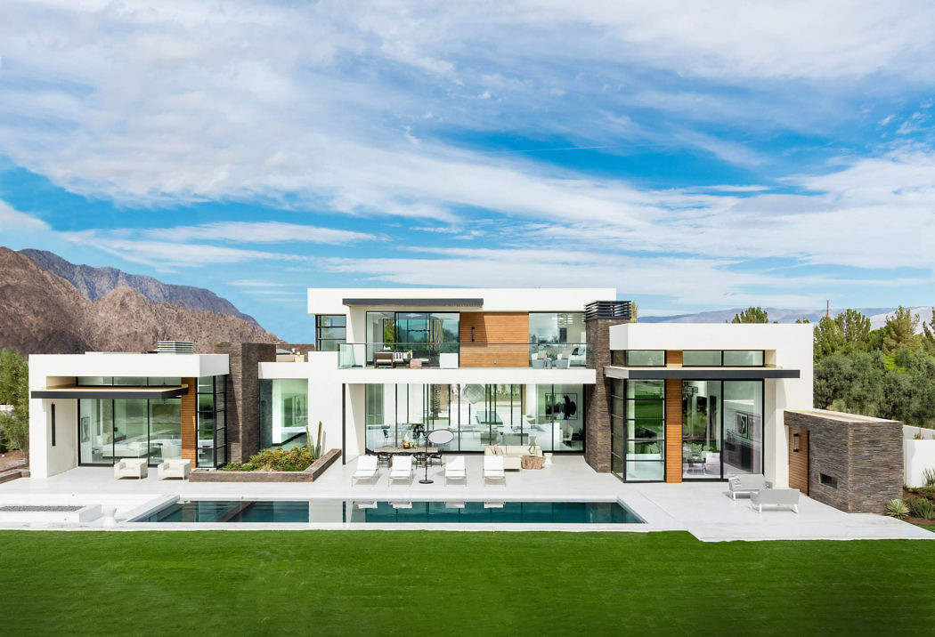 Contemporary house with large windows and a pool, set against mountains.