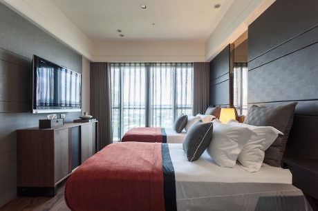 Modern hotel room with twin beds, a TV, and a large window.