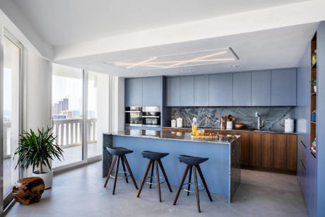 Sleek kitchen with blue cabinets and bar seating by a large window.