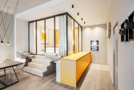 Modern apartment interior with yellow kitchen island and glass partition.