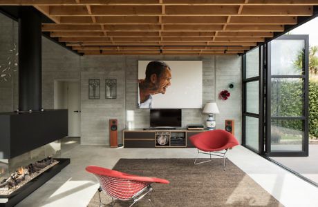 Modern living room with fireplace, red chair, and large portrait over TV.