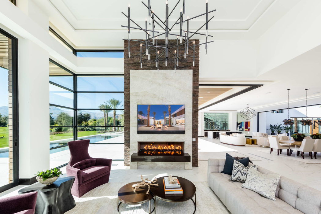 Modern living room with a fireplace, chandelier, and expansive windows.