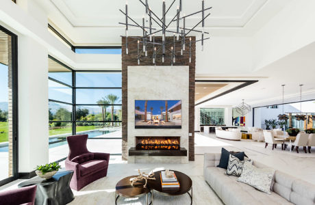 Modern living room with a fireplace, chandelier, and expansive windows.