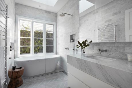 Modern bathroom with marble surfaces, freestanding tub, and window.