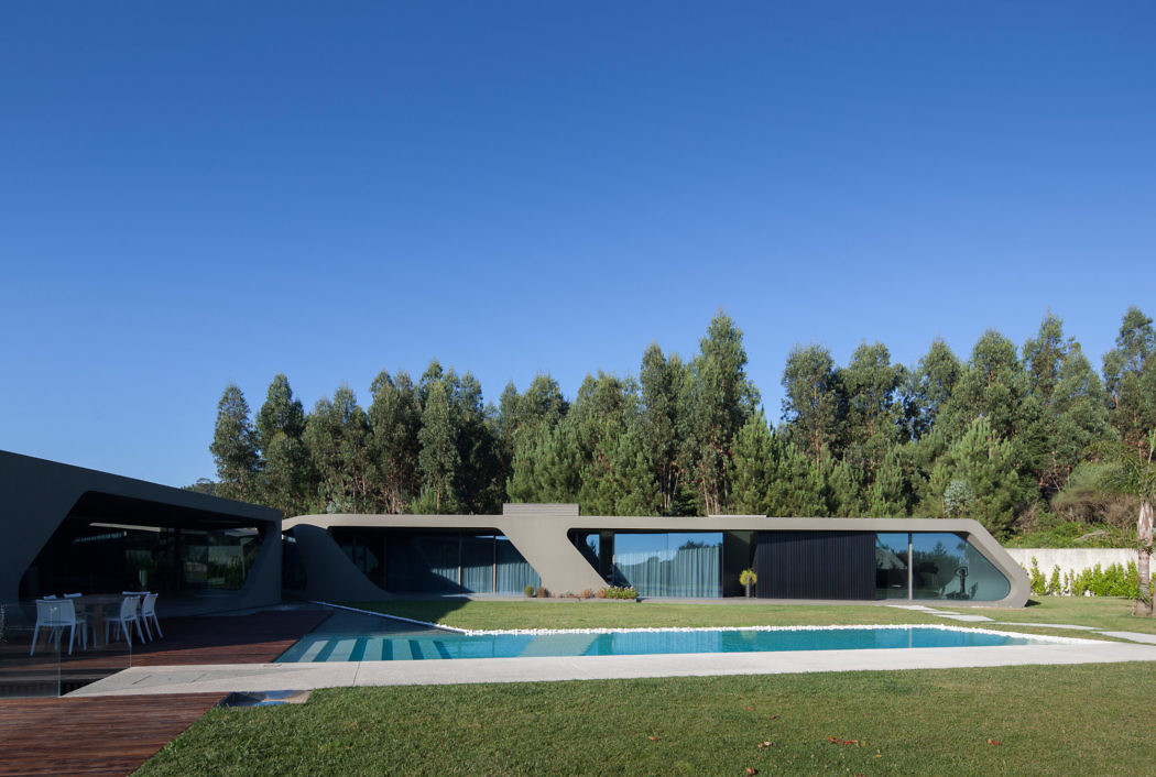 Futuristic house with curved design, pool, and greenery.