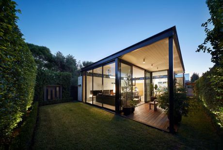 Sleek glass-walled house with a gabled roof and warm interior lighting