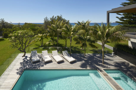Pool area with sun loungers overlooking the sea and palm trees.