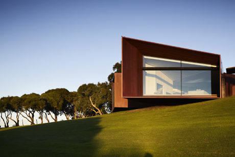 Modern house with large windows on a green hillside at dusk.