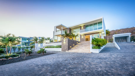 Modern two-story house with large windows at dusk, driveway in front.