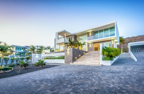 Modern two-story house with large windows at dusk, driveway in front.