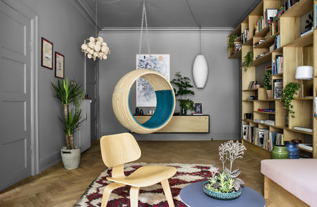 Modern living room with hanging chair, bookshelf, and wooden flooring.