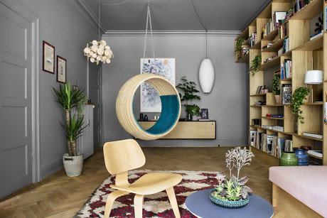 Modern living room with hanging chair, bookshelf, and wooden flooring.