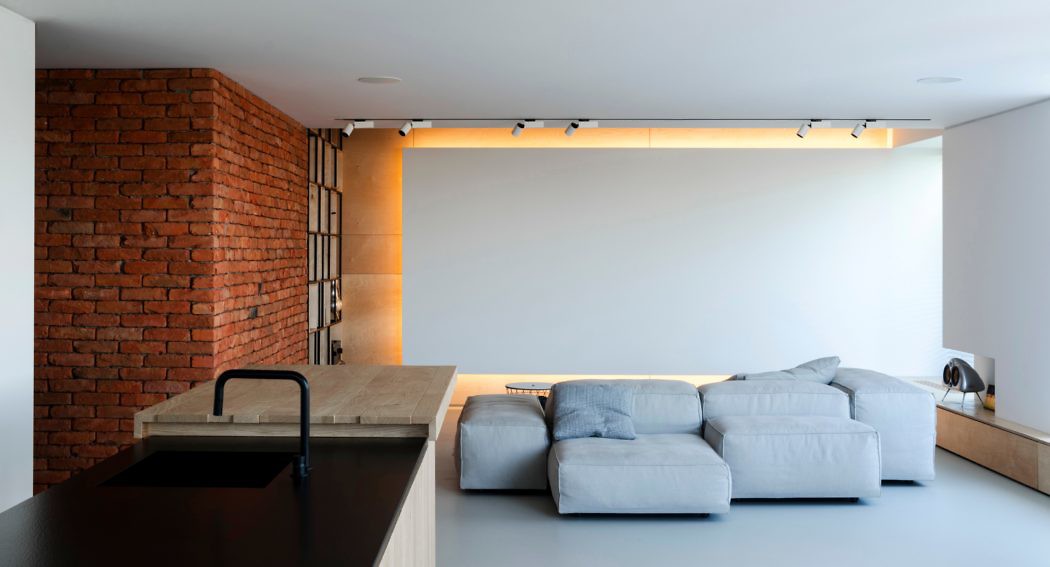 Minimalist interior with exposed brick, sleek kitchen, and plush sofa.