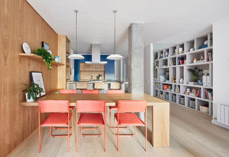 Modern kitchen with wooden dining set, blue accents, and bookshelf.