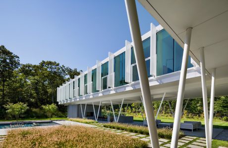 Contemporary building with white supports and extensive glass facades over a pool.