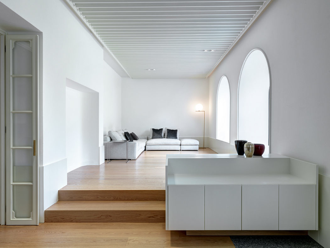 Modern living room with arched windows, white furniture, and wooden flooring.