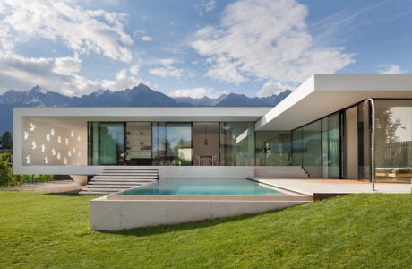 Contemporary house with large windows, pool, and mountain backdrop.